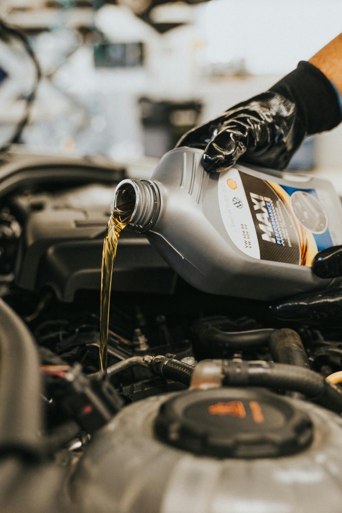 pexels-photo-13065700-13065700 Close-up of a mechanic's gloved hand pouring engine oil into a vehicle.